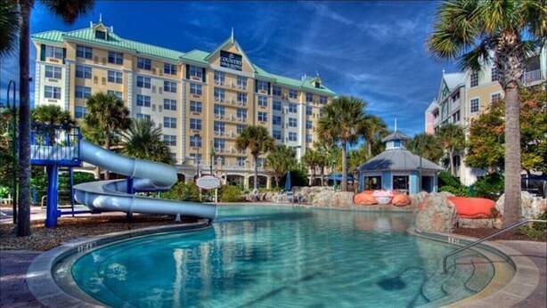 Ein Hotel mit Swimmingpool, Palmen und einem Spielplatz.