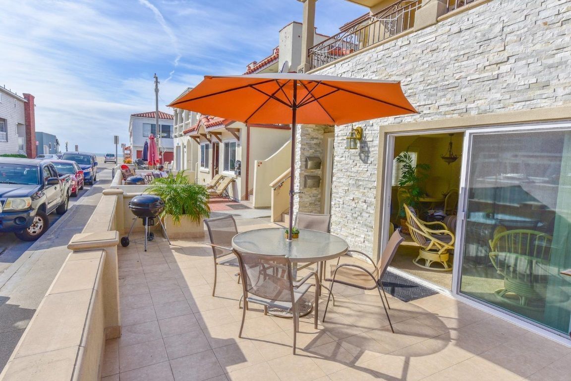 A patio with a round table and chairs, an orange umbrella, and a barbecue grill.