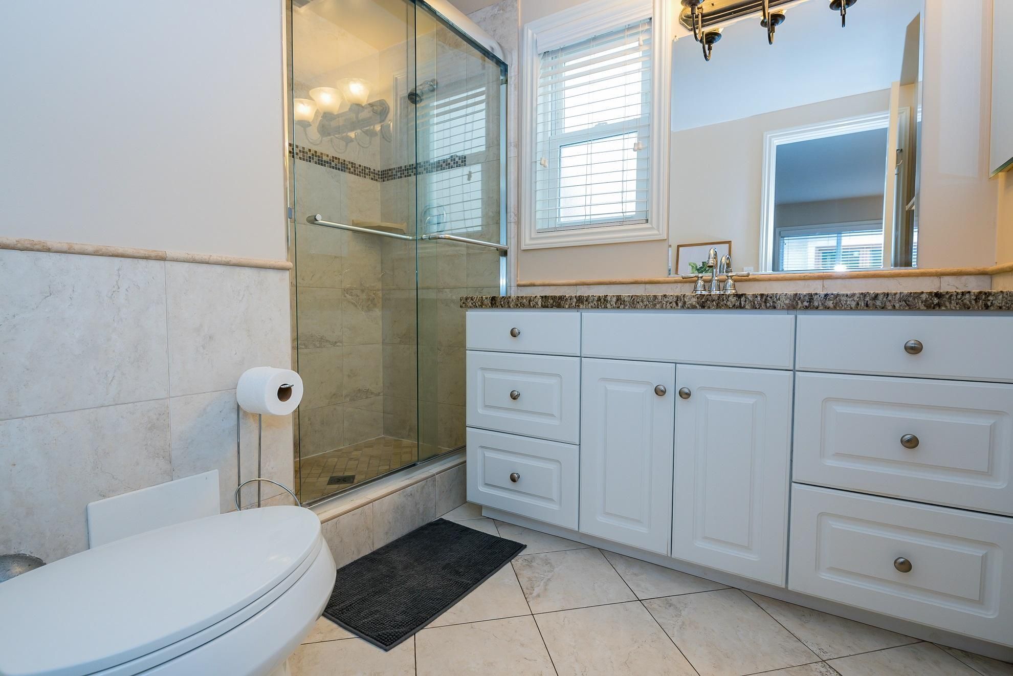 Un baño con cabina de ducha de vidrio, inodoro, lavamanos con espejo y un mueble con cajones.