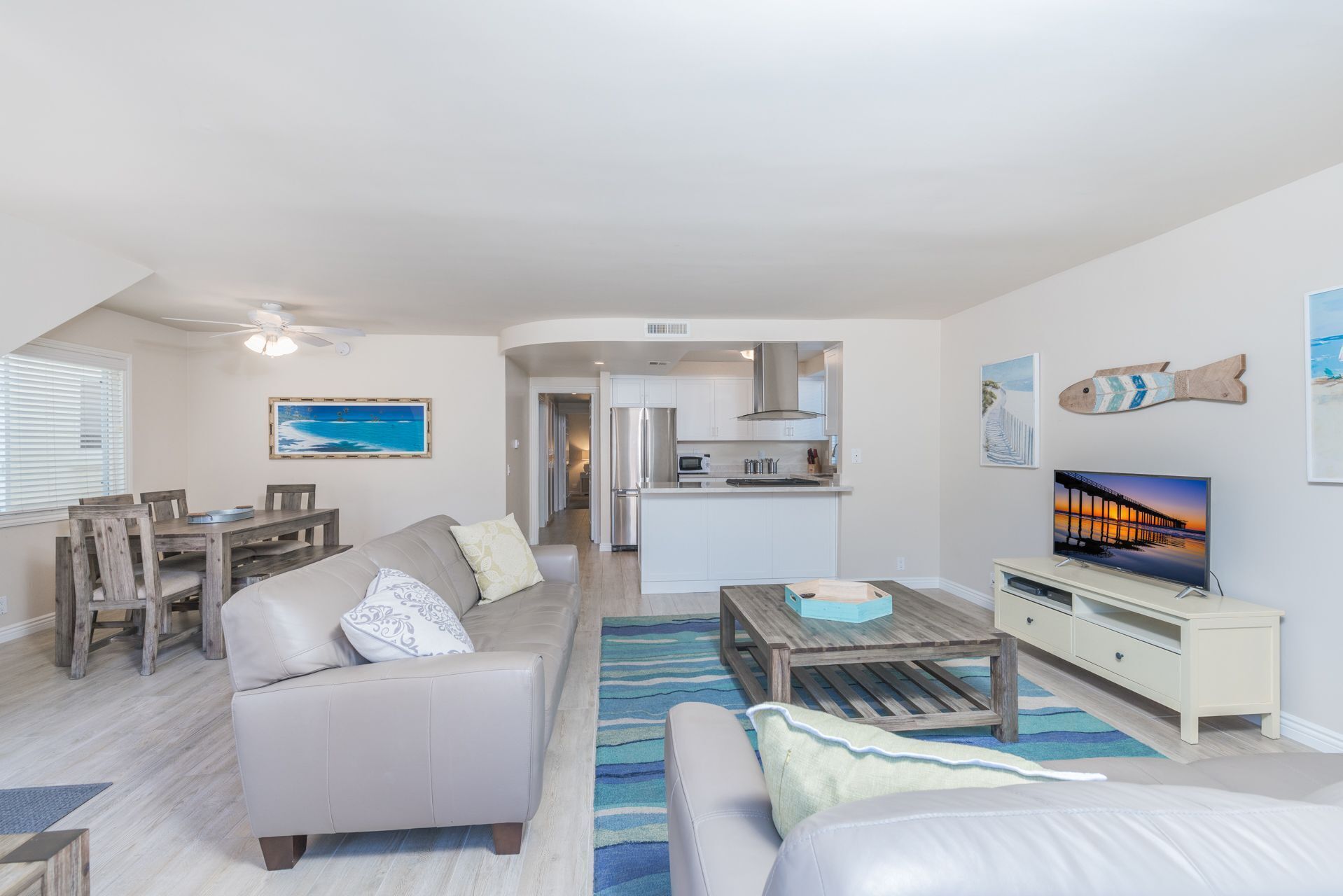 A spacious living area with a sofa, coffee table, and a TV. A kitchen is visible in the background with white cabinets and a microwave.