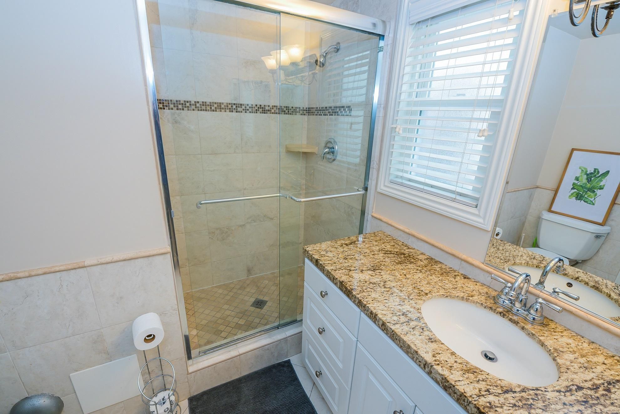 A bathroom with a glass-enclosed shower, a sink with a granite countertop, and a toilet.