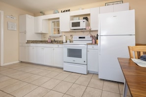 Una cocina con armarios blancos, un microondas, una estufa y un refrigerador.