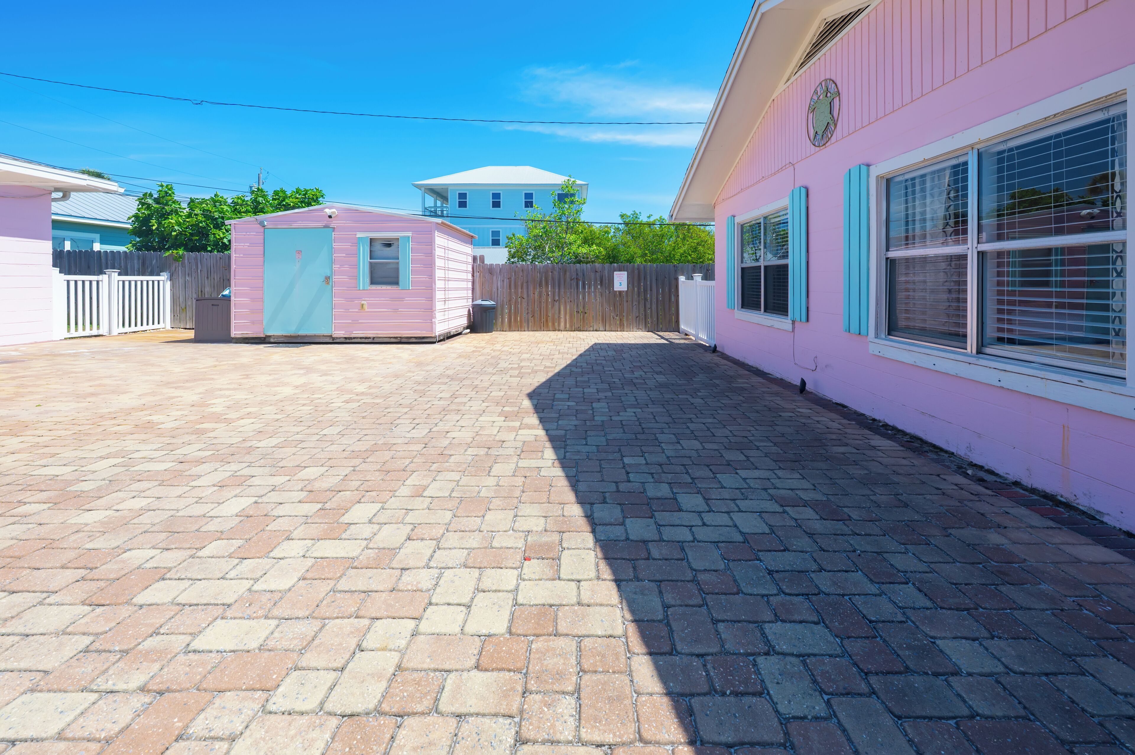 Un bâtiment rose avec une petite dépendance attenante, une cour clôturée et un chemin piétonnier dallé.