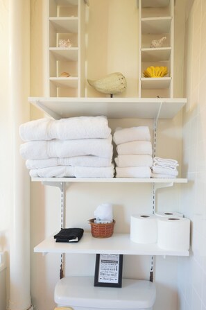 A bathroom with white shelves holding towels, a basket, and toilet paper.