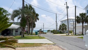 A residential street with houses, palm trees, and a clear view of the ocean.