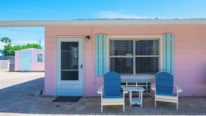A pink building with a door, two blue chairs, and a small table.