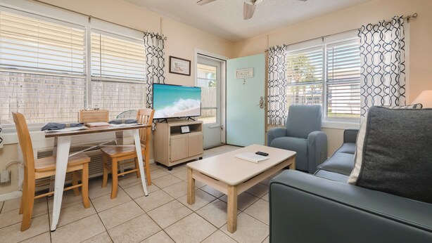 A compact living space with a dining area, a television, a sofa, and a door with a sign.