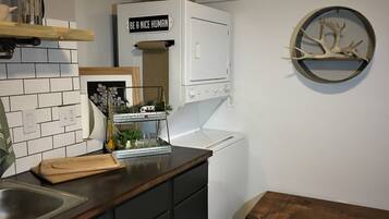 A kitchen with a white stove, a sink, and a wooden countertop. There is a basket on the wall and a shelf with a sign that says "BE A NICE HUMAN".