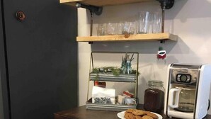 Een keuken met een zwarte koelkast, een houten plank boven het aanrecht met glazen, een koffiezetapparaat en een glazen pot.