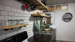 Een keuken met witte betegelde wanden, een fornuis, een spoelbak en planken met keukengerei.