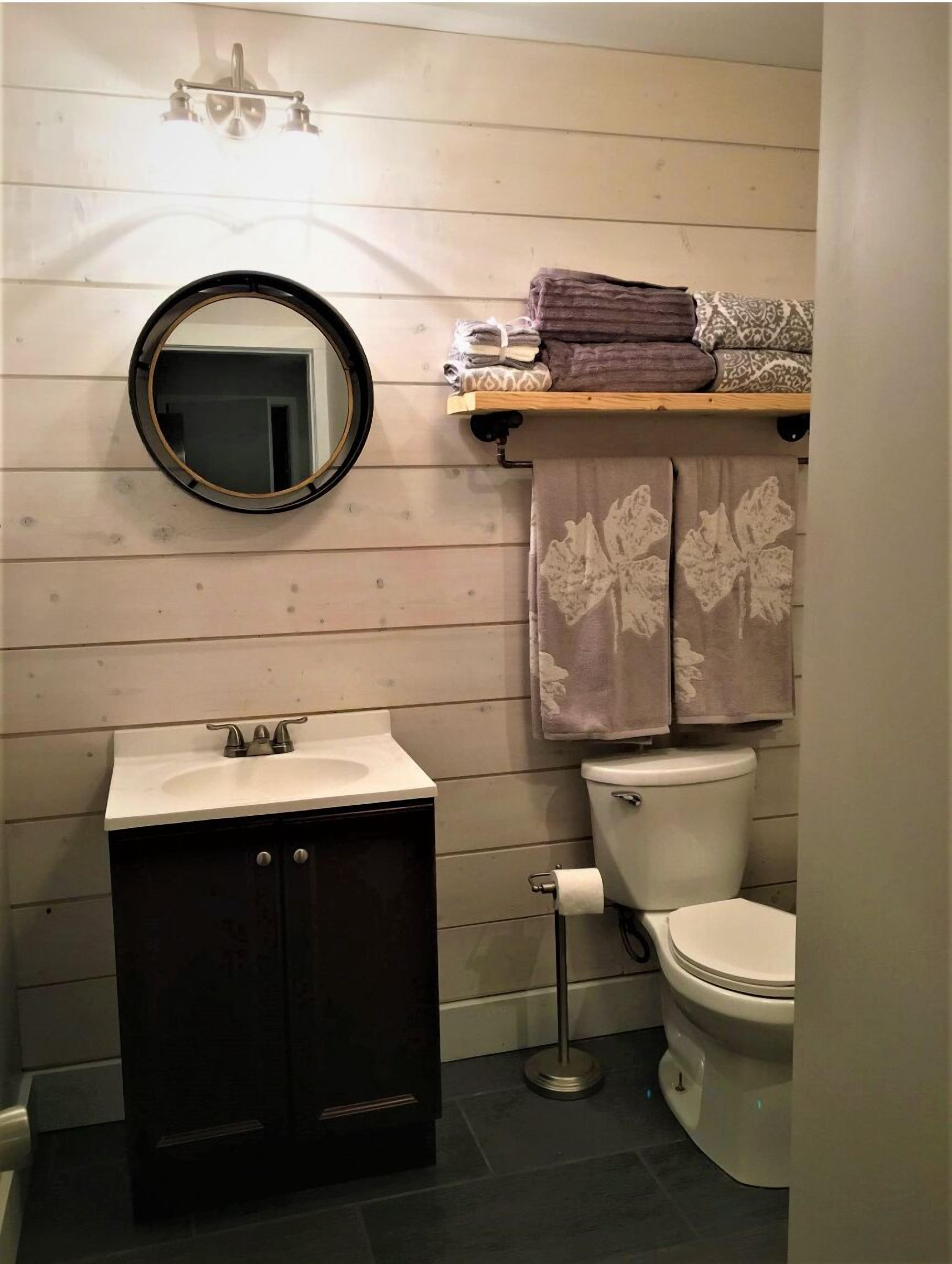 Une salle de bain avec un miroir rond, un lavabo, des toilettes et un porte-serviettes avec des serviettes pliées.