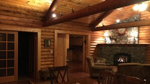 Interior acogedor de una cabaña de troncos con chimenea de piedra, vigas de madera en el techo y un comedor con un corredor rojo.