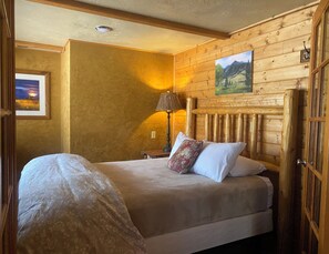 Ein gemütliches Schlafzimmer mit einem hölzernen Kopfteil, einem Bett mit floralem Bettzeug, einem Nachttisch mit Lampe und einem Bild an der Wand.