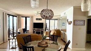 A dining area with a round glass table, chairs, a central vase, and a television in the background. - Direct Gulf Front View And Your Very Own Private Pier 504W (Orange Beach)
