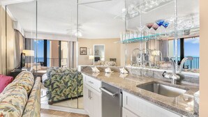 A modern kitchen with a granite countertop, stainless steel sink, and glass shelving with decorative items. - Direct Gulf Front View And Your Very Own Private Pier 504W (Orange Beach)