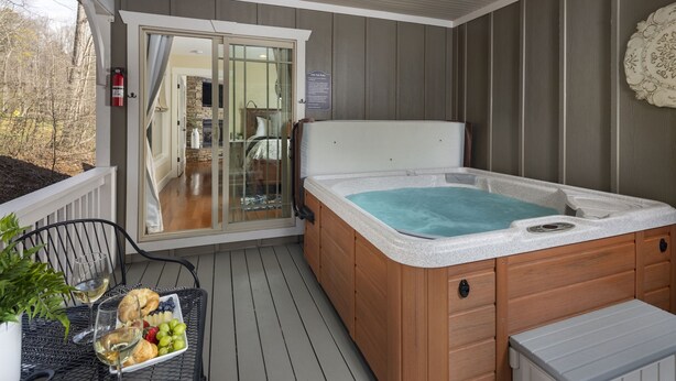 A hot tub on a wooden deck with a glass door leading to a stone fireplace. - Family-Run Cottage with Fireplace and Private Hot Tub (Asheville)