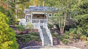 A cabin with a wooden staircase leading to a porch, surrounded by dense forest. - Family-Run Cottage with Fireplace and Private Hot Tub (Asheville)