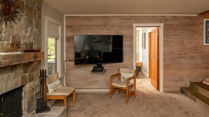 A living room with a stone fireplace, a flat-screen TV mounted on the wall, and a wooden door leading to another room. - Snow Creek Condo with 2 Bedrooms, 2 Bathrooms and expanded ground level patio !! (Sun Valley)