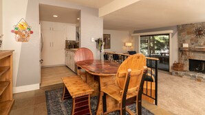 A dining area with a wooden table and chairs, a kitchen in the background, and a stone fireplace. - Snow Creek Condo with 2 Bedrooms, 2 Bathrooms and expanded ground level patio !! (Sun Valley)