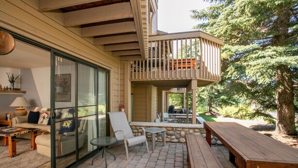 A covered outdoor patio with a wooden deck, seating area, and a stone wall. - Snow Creek Condo with 2 Bedrooms, 2 Bathrooms and expanded ground level patio !! (Sun Valley)