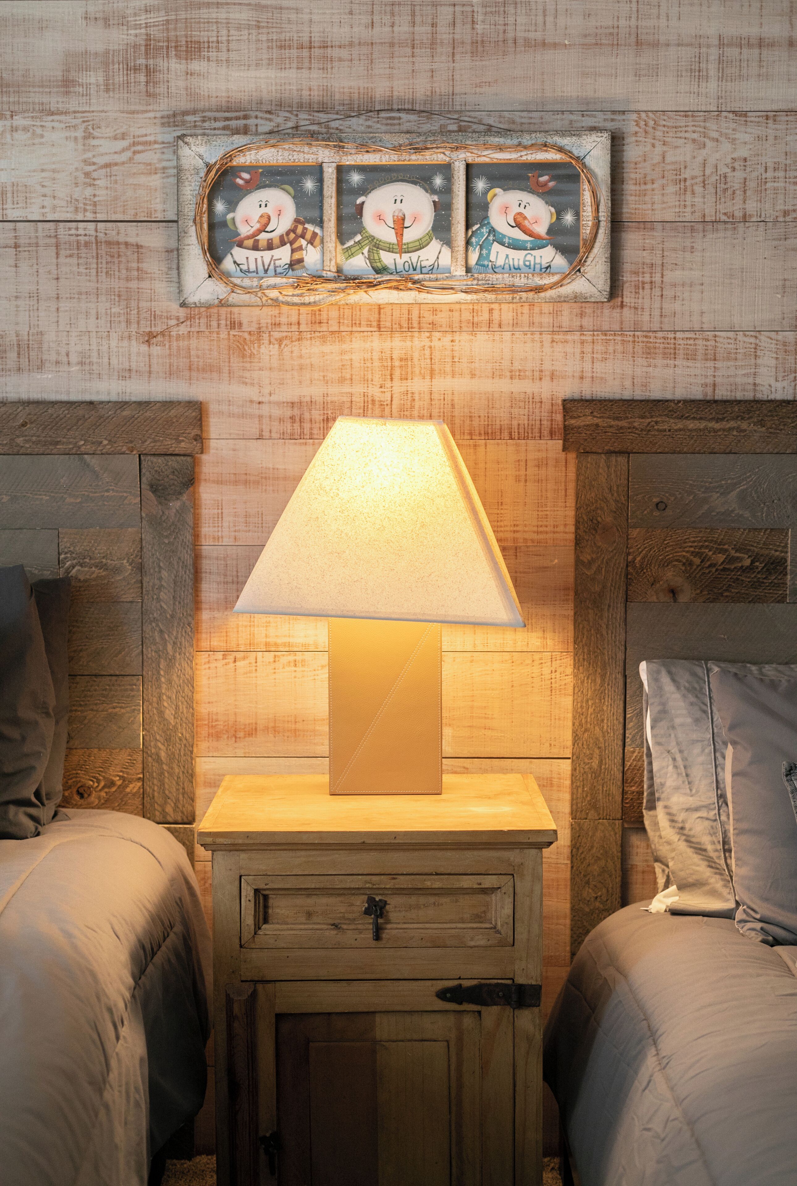A bedroom with a wooden nightstand, a lamp, and three wall decorations.