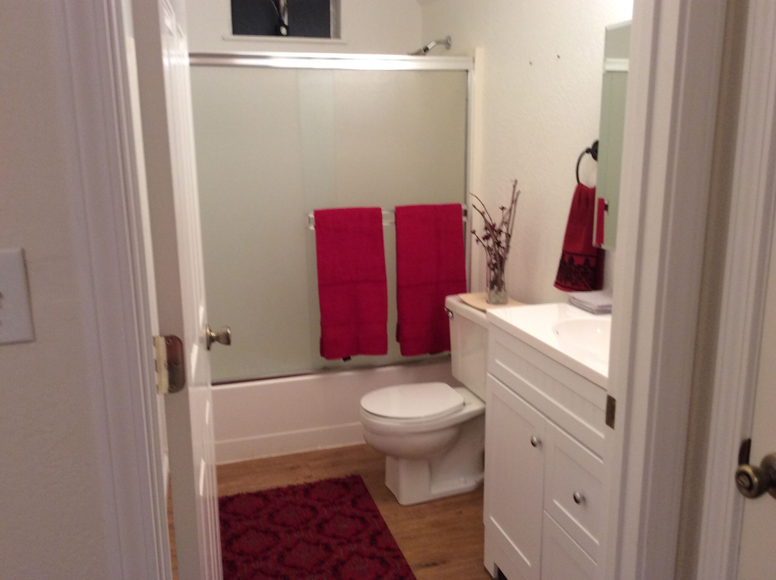 Un baño con un inodoro blanco, una bañera y una ducha. Hay dos toallas rojas colgadas en la pared.