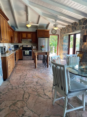 A spacious kitchen with wooden cabinets, a central island, and a dining area with a glass table and chairs.
