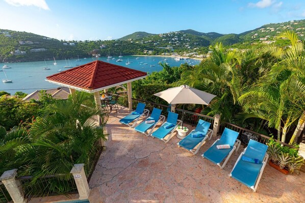 A rooftop terrace with lounge chairs and a dining area overlooking a bay with boats.