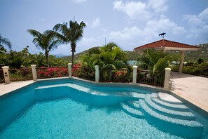 A swimming pool with clear blue water, surrounded by tropical plants and a gazebo.