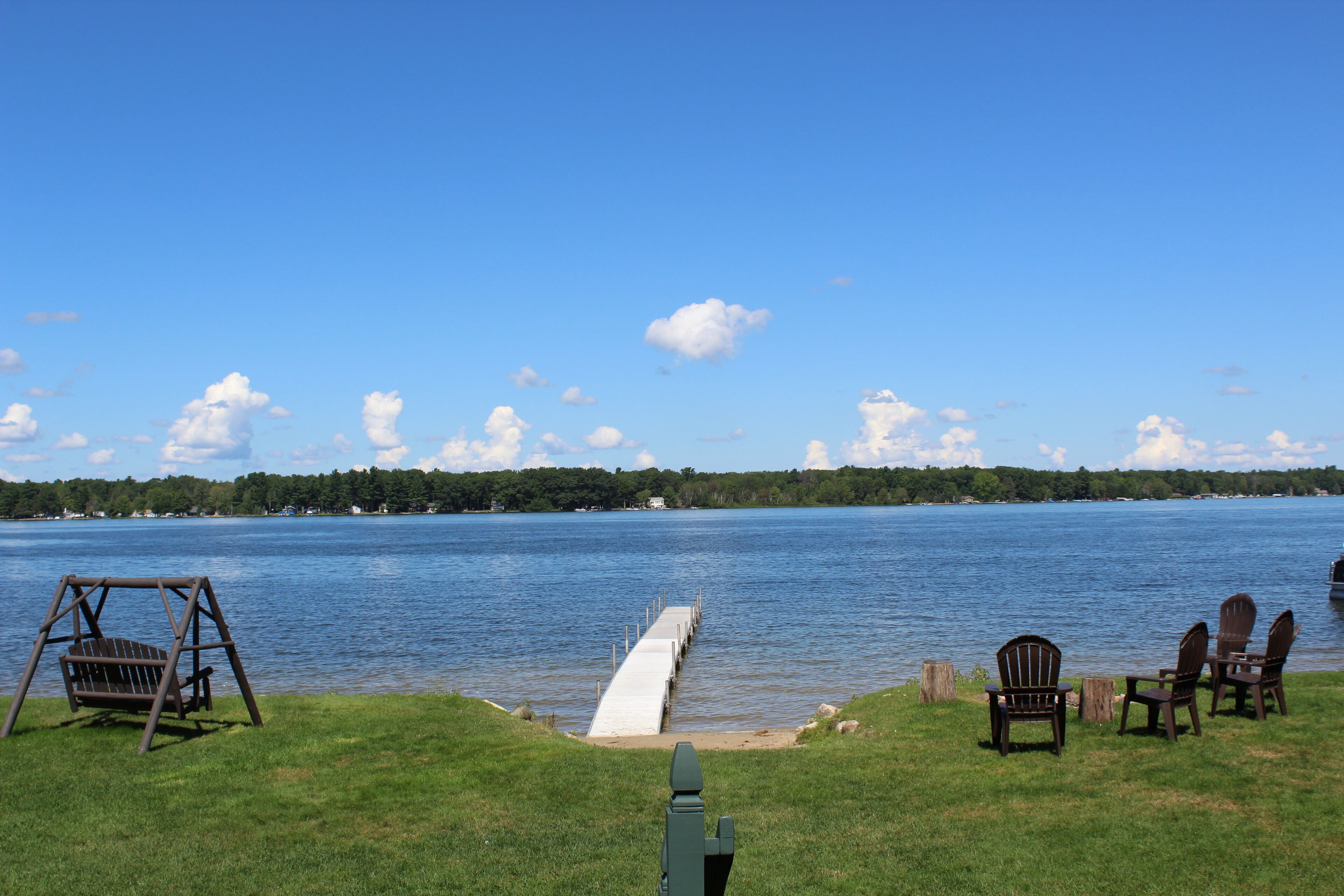 Une vue sur le lac avec une balançoire en bois, un quai et des fauteuils Adirondack.