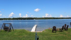 A lakeside view with a wooden swing, dock, and Adirondack chairs.