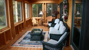 A wooden cabin with a cozy interior, featuring wicker furniture, a glass coffee table, and a view of the surrounding forest.