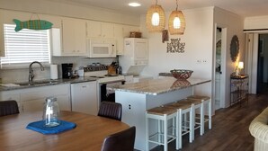 Une cuisine moderne avec des meubles blancs, un îlot central doté de tabourets, un four à micro-ondes, une cuisinière et des luminaires suspendus.