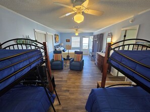 Ein Zimmer mit Etagenbetten, einem Schreibtisch, Stühlen und einem Deckenventilator.
