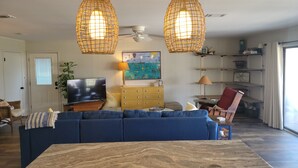 Un salon avec un canapé bleu, une table basse en bois et deux suspensions en rotin.