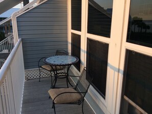 A balcony with a round table and two chairs, large windows, and a white railing.