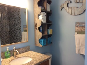 A bathroom with a granite countertop, a sink, a mirror, a towel rack, and a shelf with toiletries.