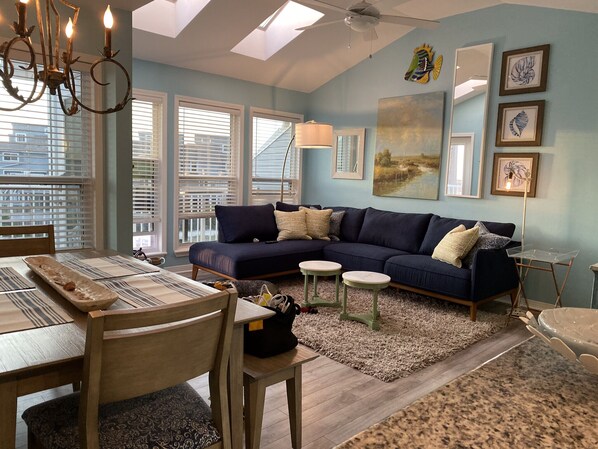 A living room with a dark blue sofa, a dining table with chairs, a chandelier, and artwork on the walls.