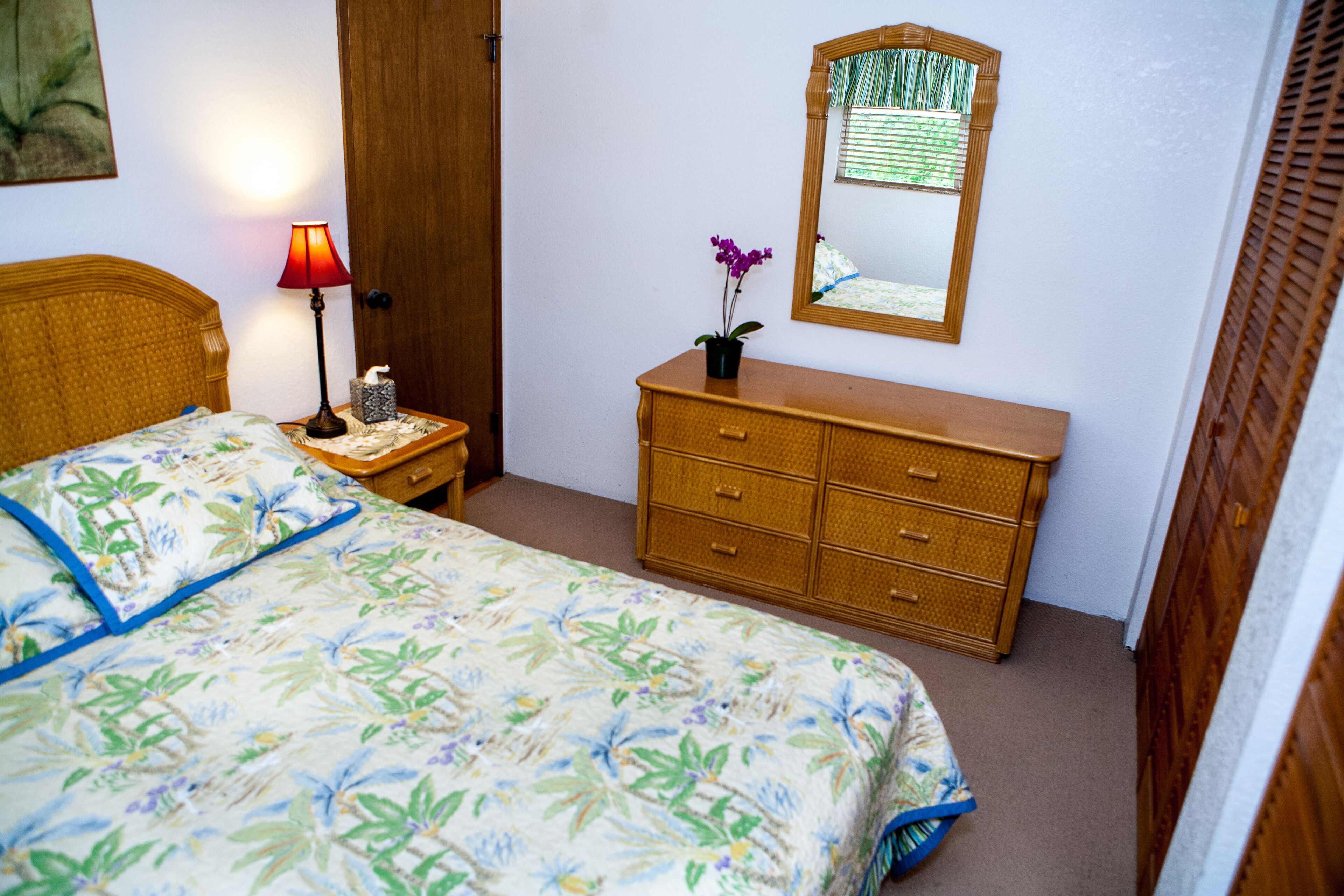 Une chambre à coucher avec un lit, une table de chevet, une commode, un miroir et une porte.