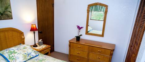 Une chambre à coucher avec un lit, une table de chevet, une commode, un miroir et une porte.
