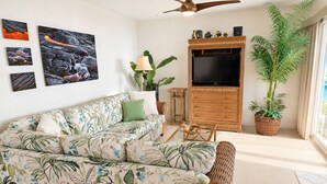 Ein Wohnzimmer mit einer Couch, einem Fernseher, einem Deckenventilator und einer Topfpflanze.