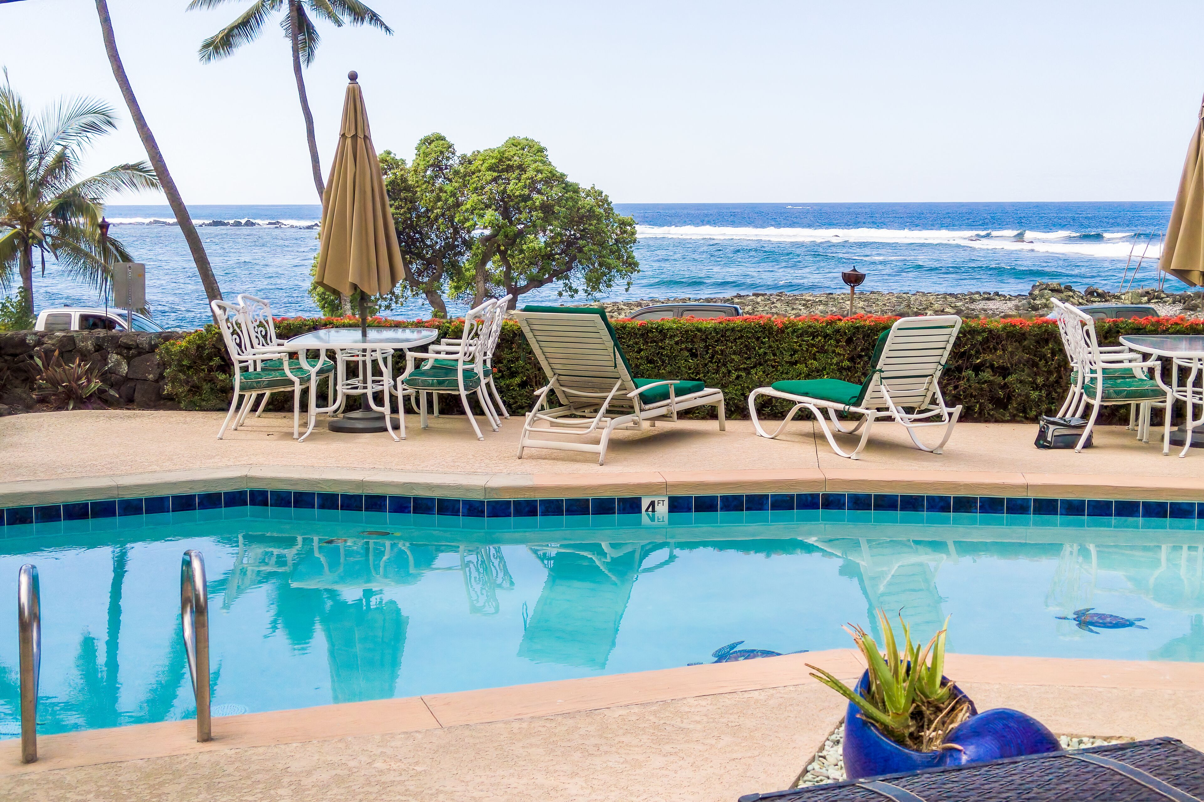 A poolside area with lounge chairs and umbrellas, a clear view of the ocean, and a tiled pool.