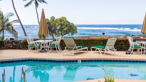 Ein Poolbereich mit Liegestühlen und Sonnenschirmen, mit Blick auf das klare Meer und einem gefliesten Pool.