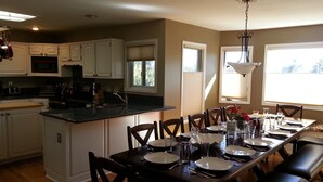 A kitchen with white cabinets, a dining table set for four, and a large window providing natural light. - Spacious Home in Quiet Area - Minutes to Attractions, Music, Restaurants & USAFA (Colorado Springs)