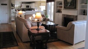A spacious living room with a high ceiling, a fireplace, and a kitchen in the background. - Spacious Home in Quiet Area - Minutes to Attractions, Music, Restaurants & USAFA (Colorado Springs)