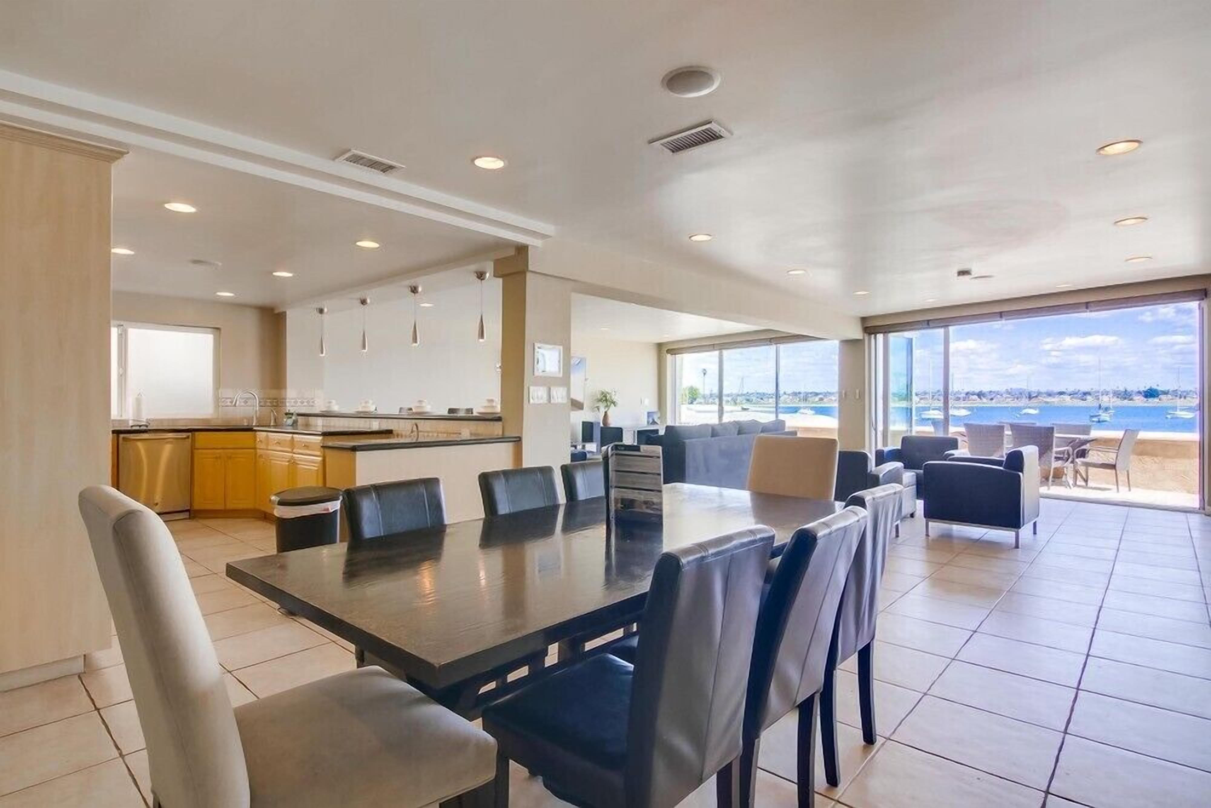 A spacious living area with a large dining table, comfortable seating, a kitchen, and a balcony with a view.