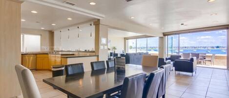 A spacious living area with a large dining table, comfortable seating, a kitchen, and a balcony with a view.