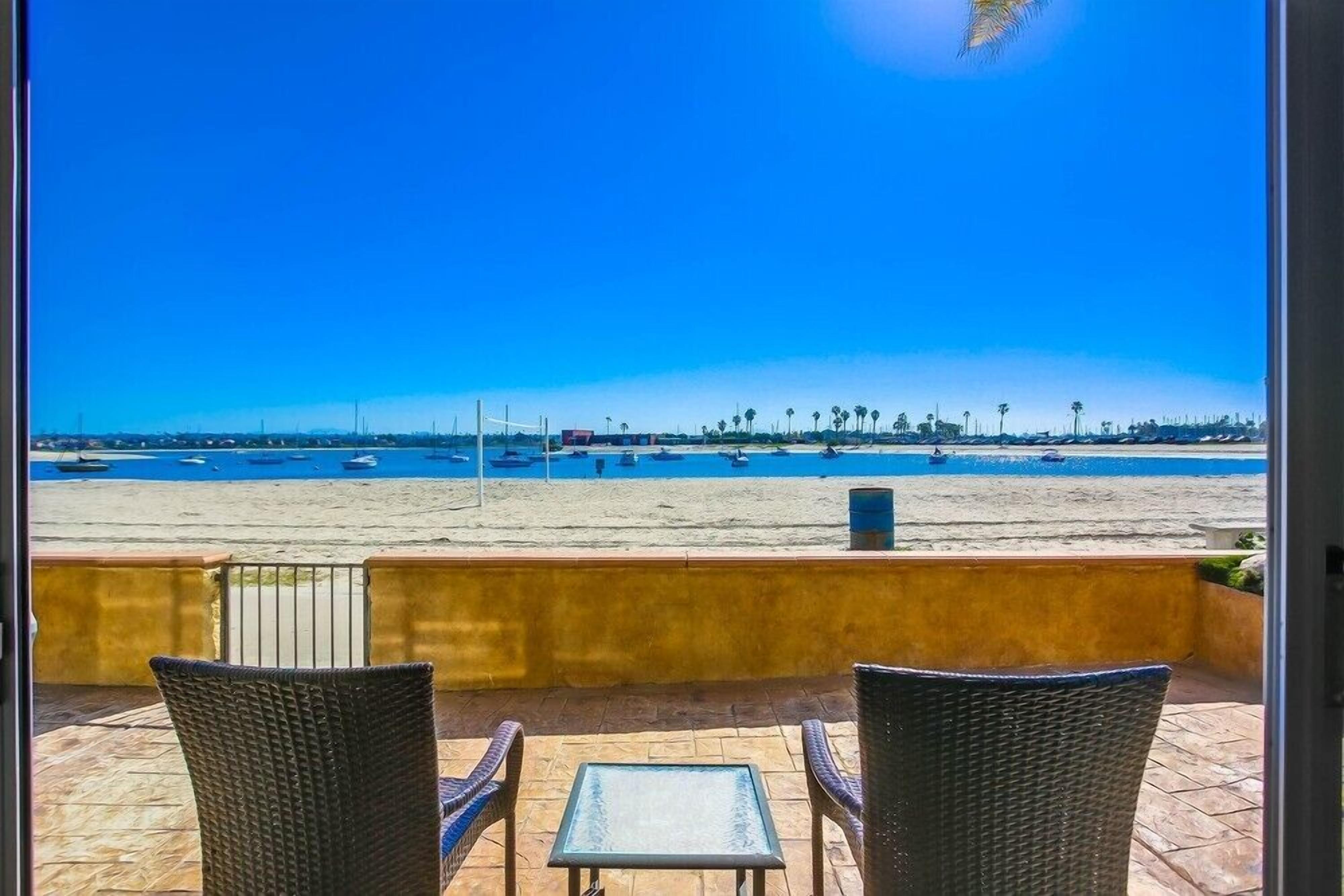 Blick auf den Strand von einem Balkon mit Korbstühlen und einem kleinen Tisch.