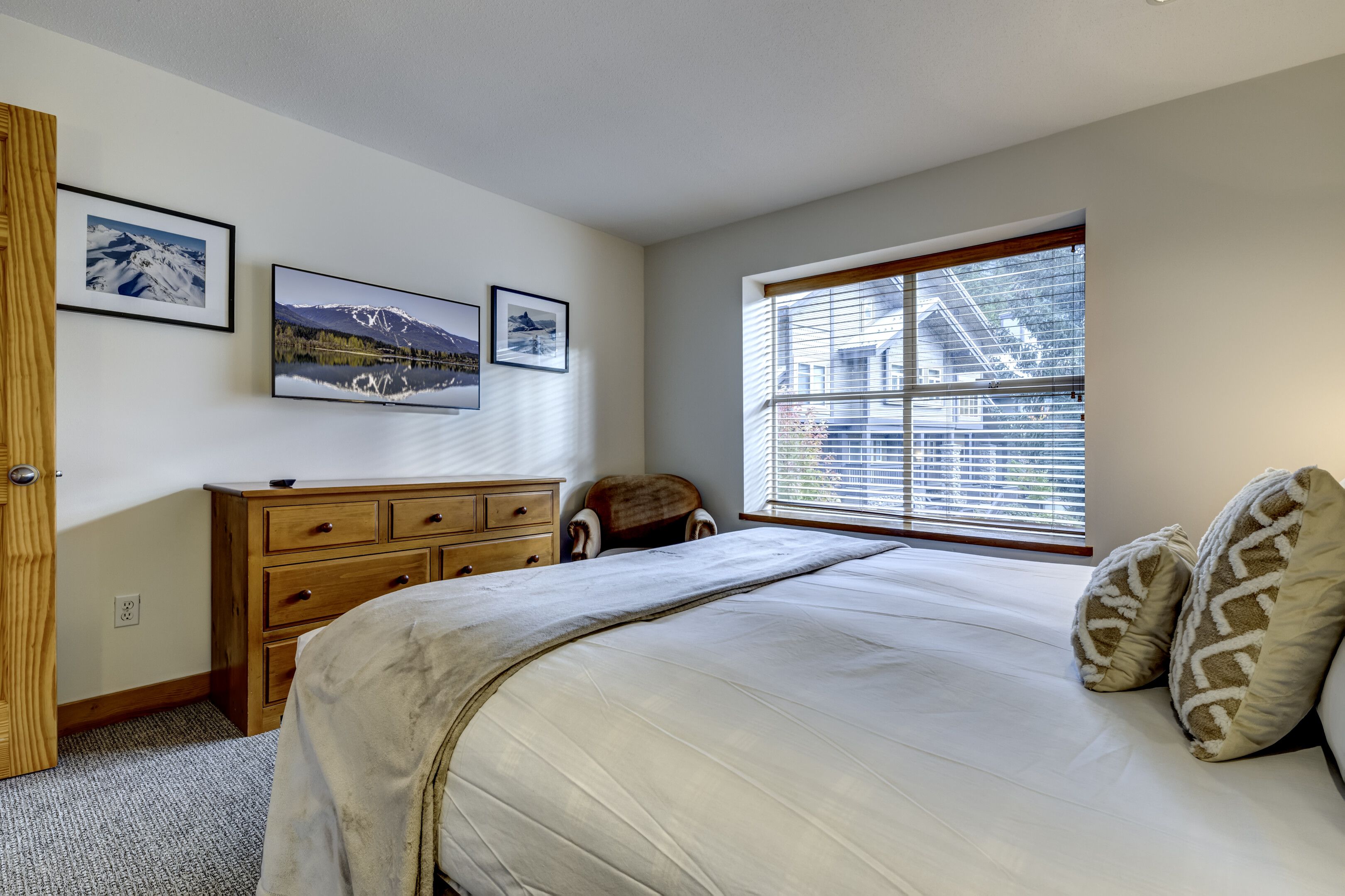 A bedroom with a bed, a dresser, a window with blinds, and framed pictures on the wall.