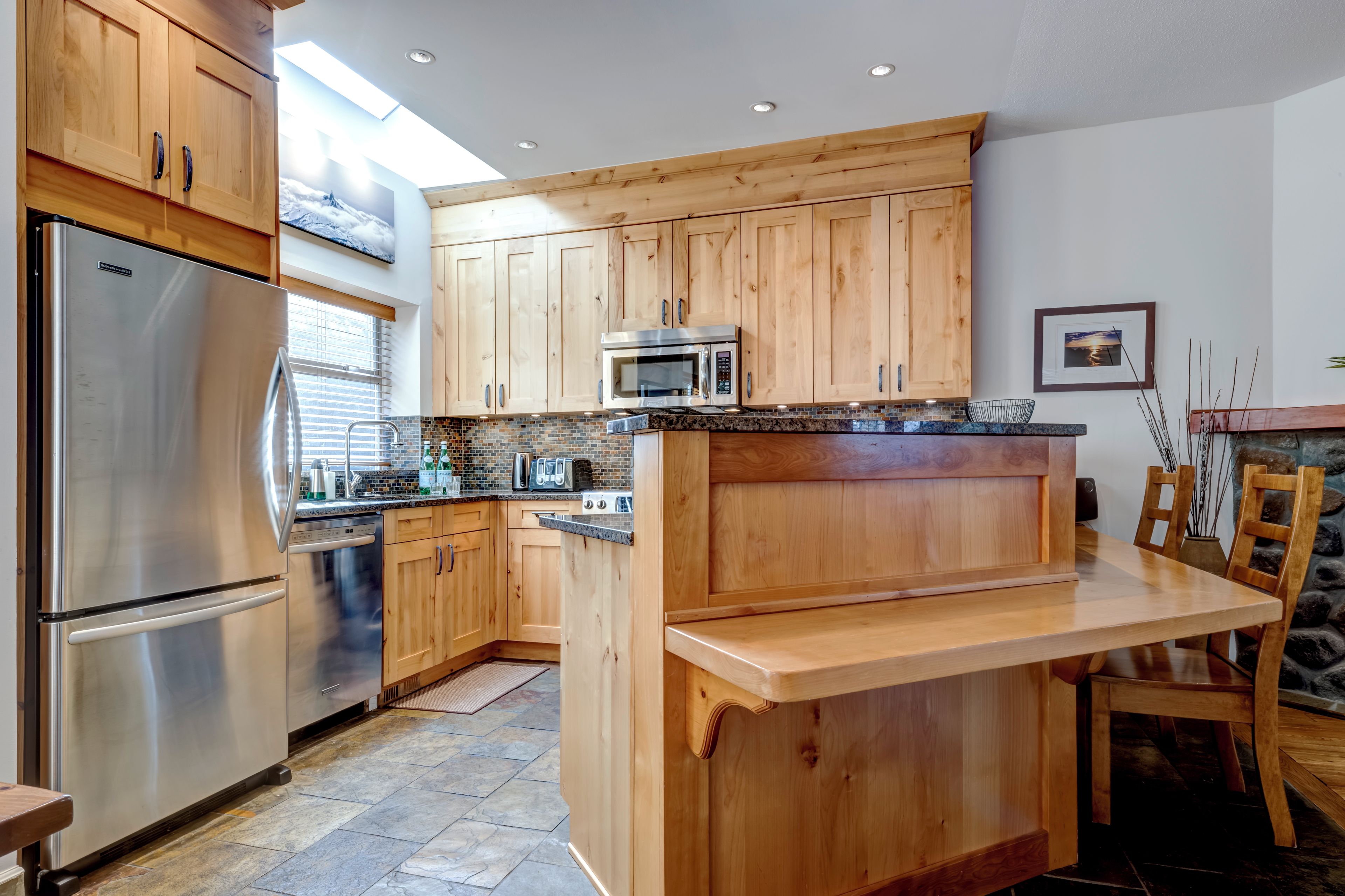 Una cocina moderna con armarios de madera, electrodomésticos de acero inoxidable y salpicadero de piedra.